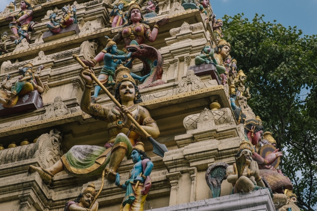 An intricately detailed façade of a Hindu temple, adorned with a vibrant array of statues depicting various deities and mythical figures in mid-narrative pose.